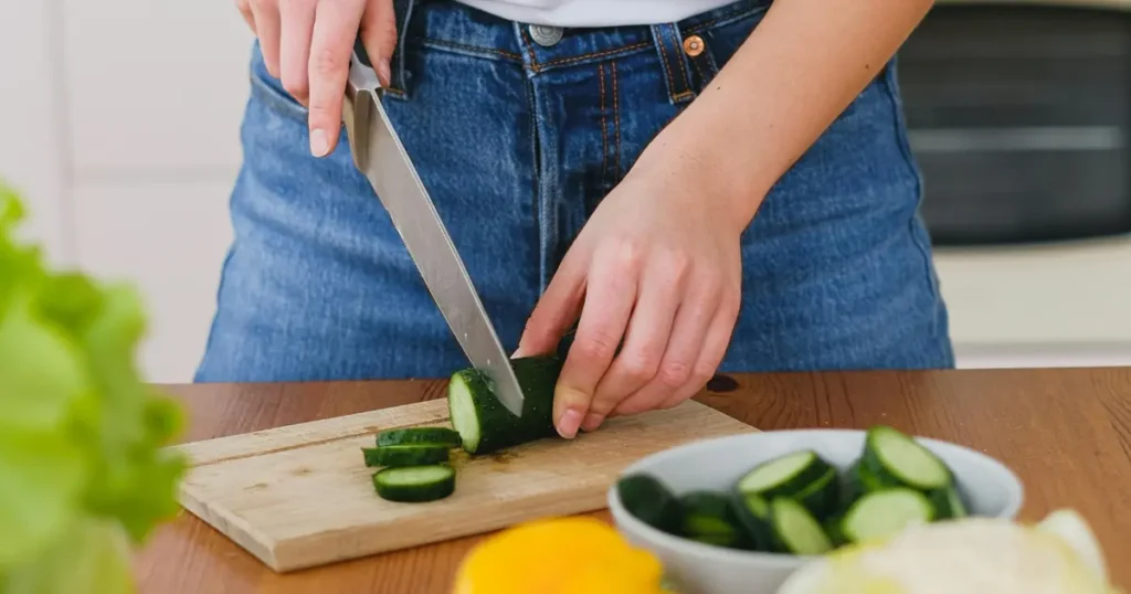 Mulher cortando pepino em uma tábua para uma alimentação saudável