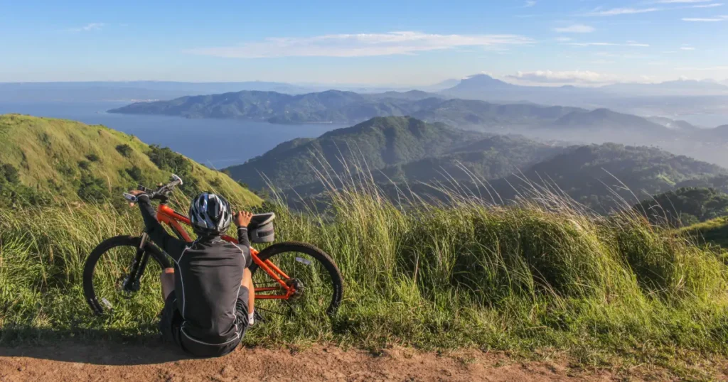 Um homem sentado na grama em uma montanha com uma bicicleta
