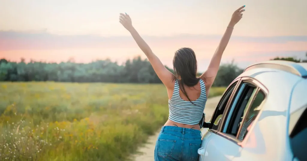Mulher ao lado de um carro com as mãos para cima