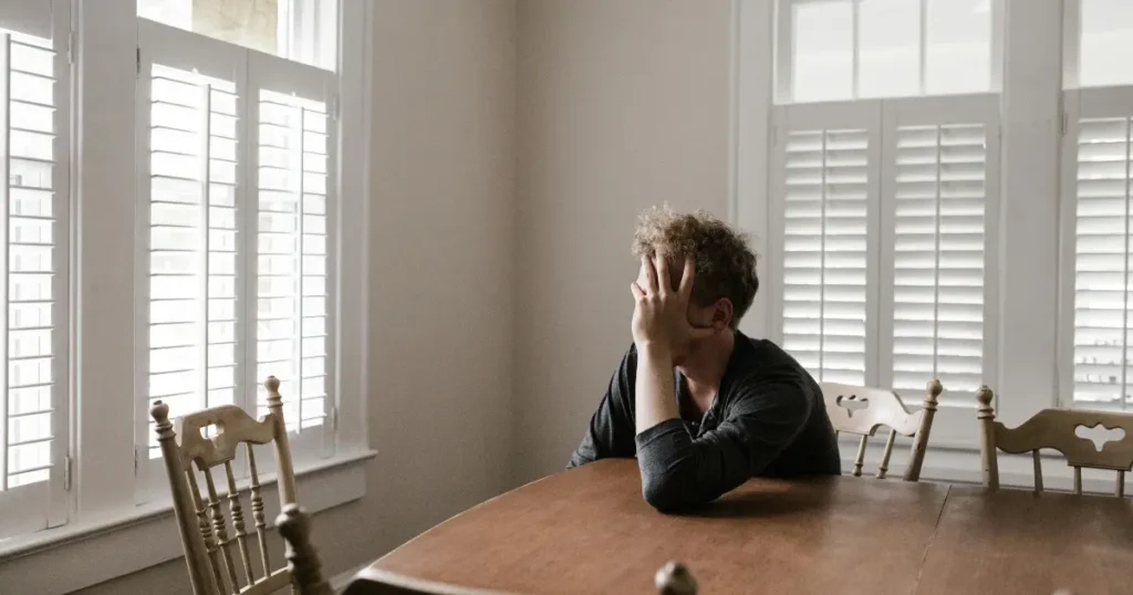 Homem sentado sobre a mesa com a mão no rosto