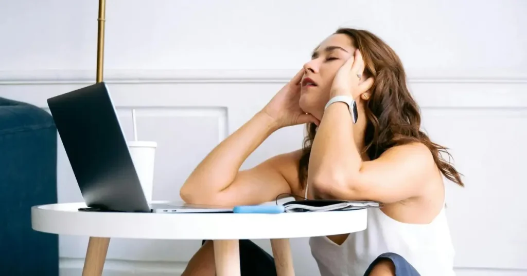 Mulher sentado no chão de frente para o computador com a mãos no rosto