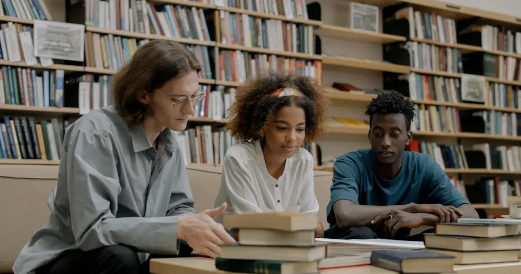 Dois homens e uma mulher lendo um livro juntos em uma bibiloteca fazendo a leitura de livros