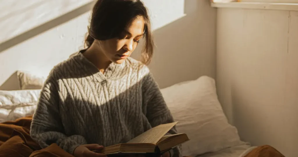 mulher sentada na cama com um semblante triste olhando para um livro