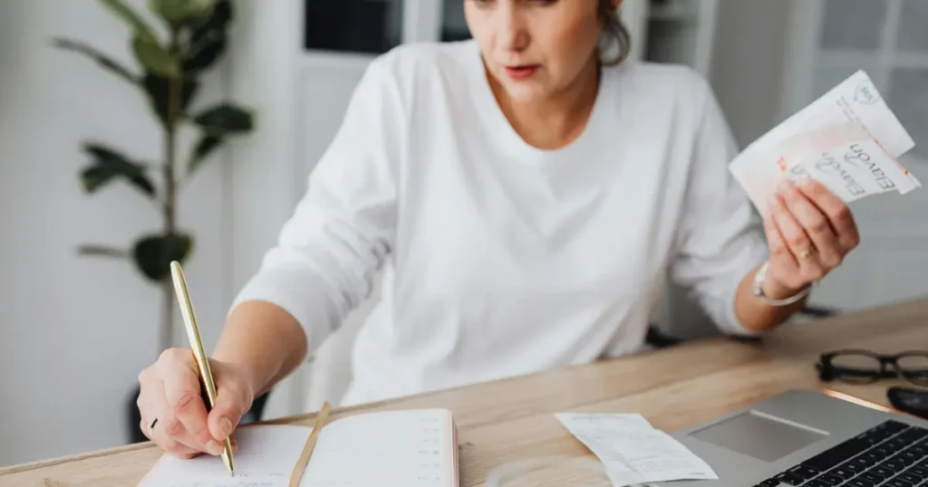 Mulher a mesa fazendo conta em um caderno