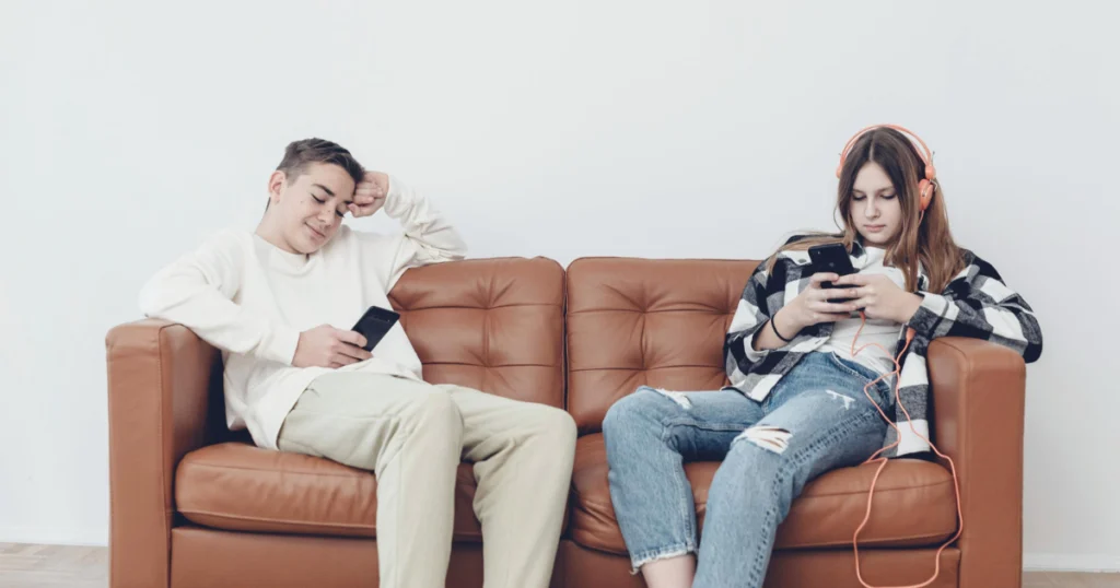 Um menino e uma menina sentados no sofá mexendo no celular